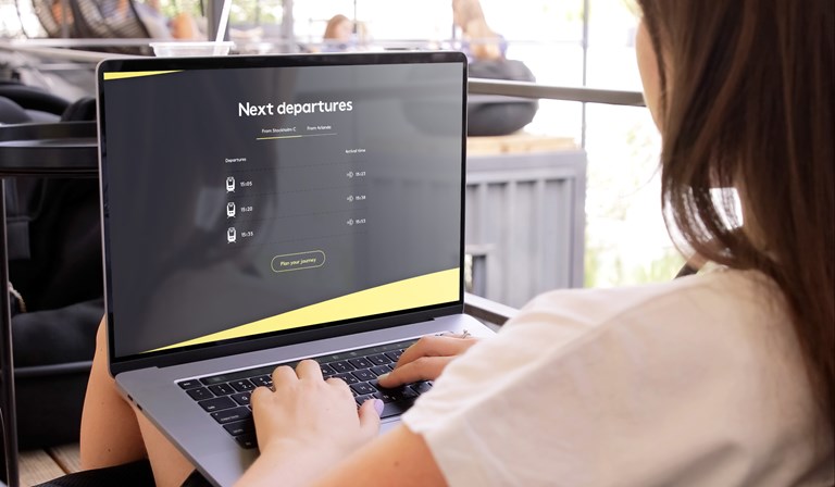 Person using a laptop displaying a travel webpage with next train departures from Stockholm C and Arlanda.