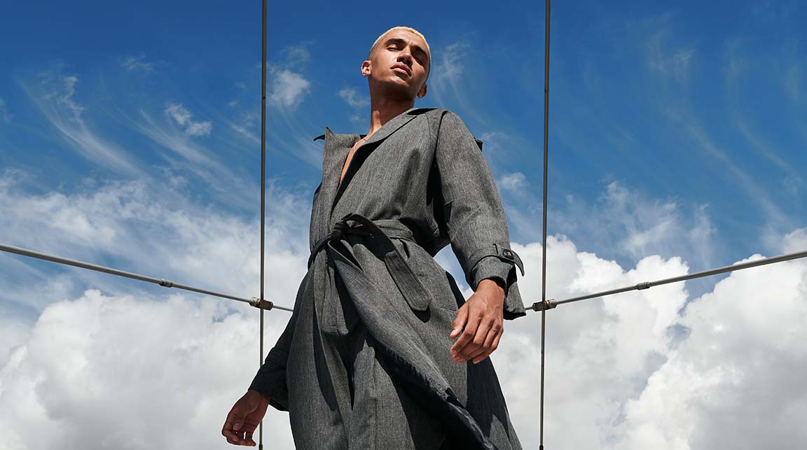 Surrealistic image of a Black man in a gray luxury suit looking towards deep blue sky