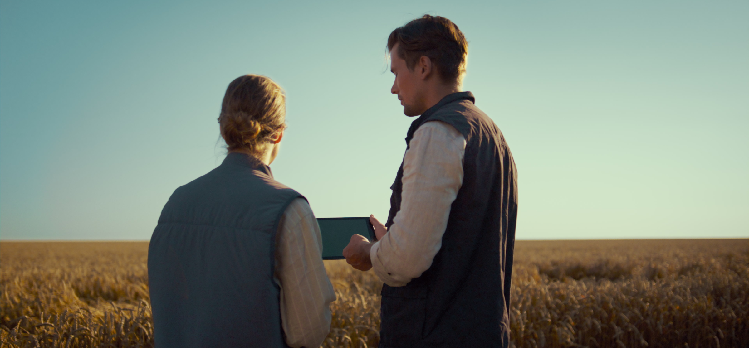 two farmers in a wheat field, one holding a tablet