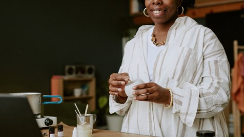 A woman is smiling as she works on making a candle.