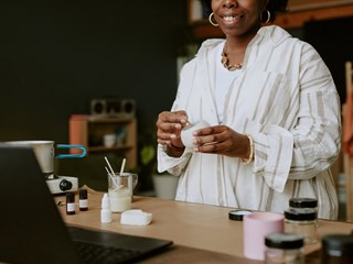 A woman is smiling as she works on making a candle.