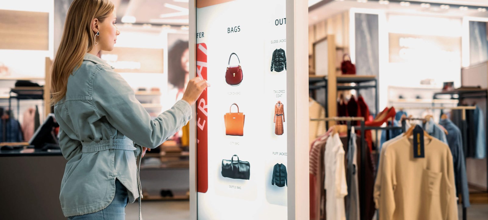 Woman using an interactive digital kiosk to browse handbags in a modern retail store.