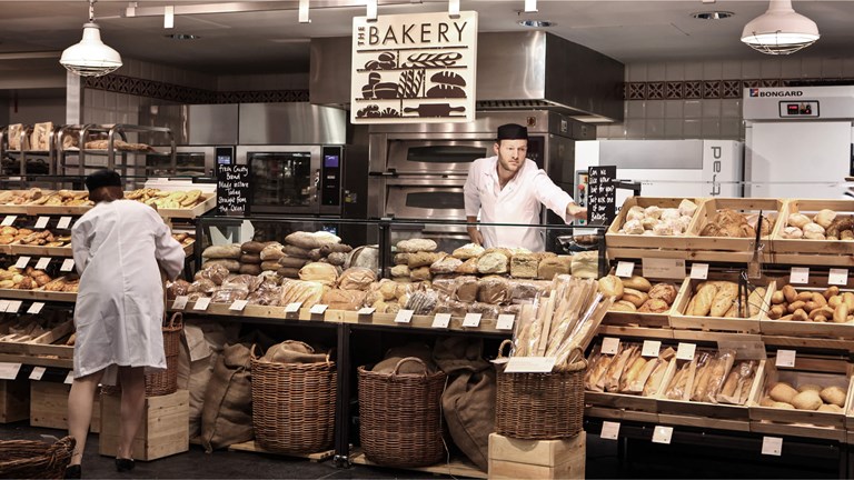 Two bakery workers are busy in a well-stocked bakery.