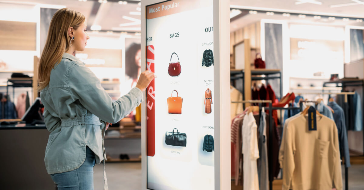 Woman using an interactive digital kiosk to browse handbags in a modern retail store.