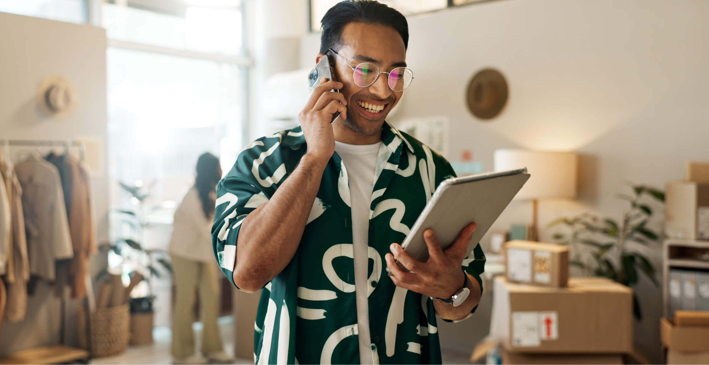 Smiling professional managing online business operations using a tablet and phone in a modern workspace.