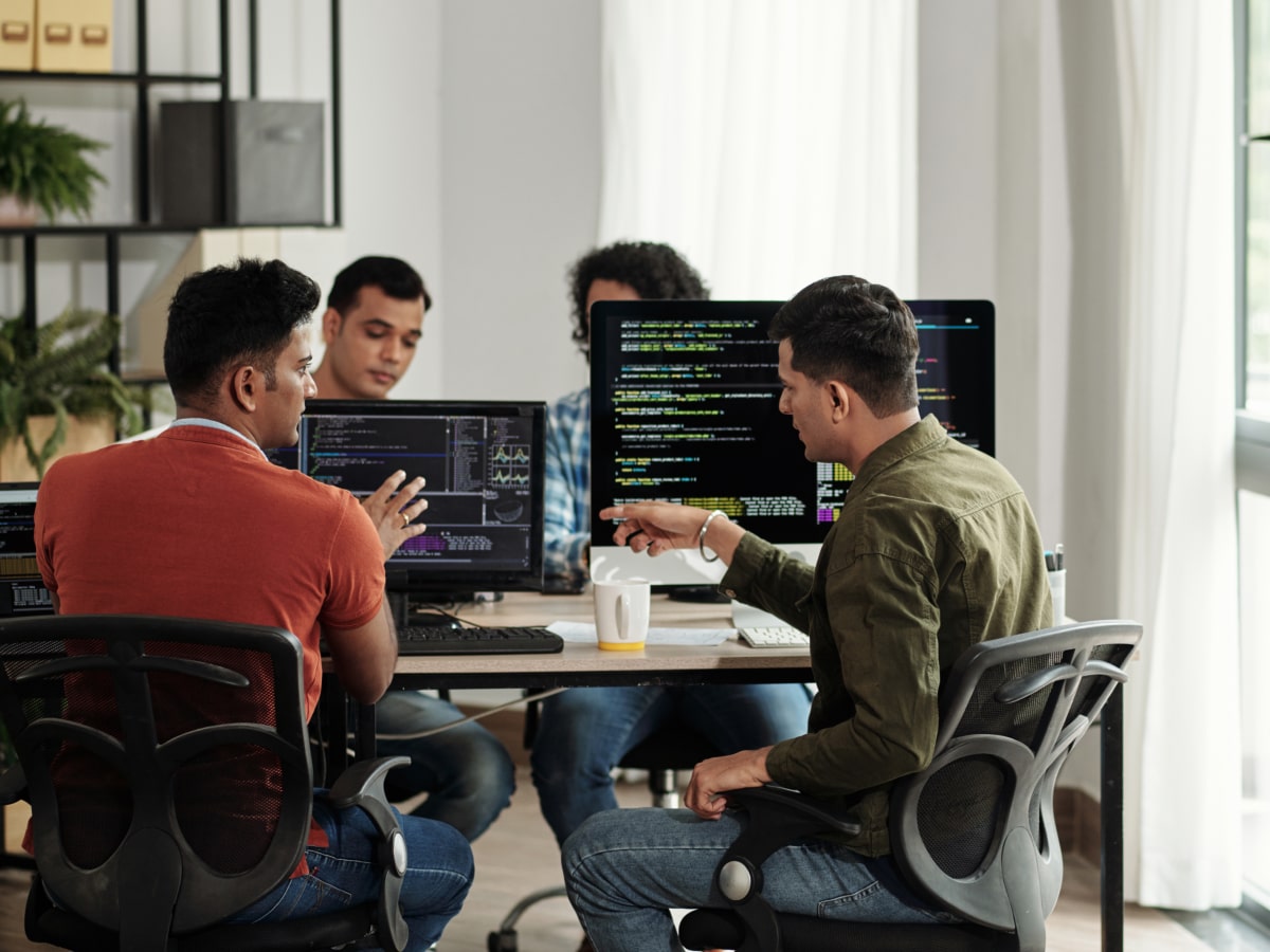 Three men seated at a table, each using a computer, engaged in a collaborative work environment.