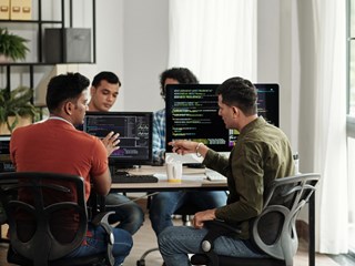 Three men seated at a table, each using a computer, engaged in a collaborative work environment.