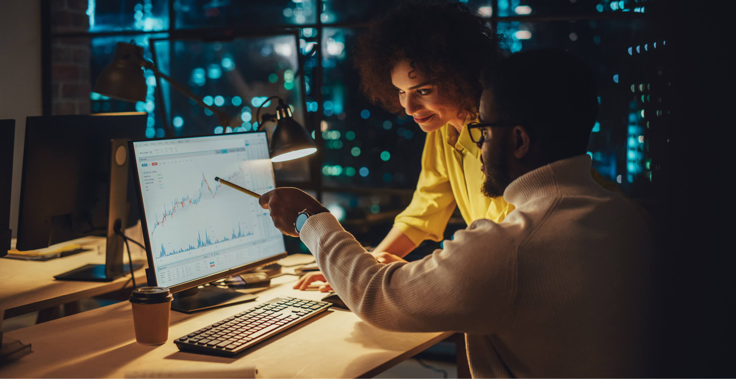 Team collaborating on financial analysis in a dimly lit office with computer screens displaying data charts.