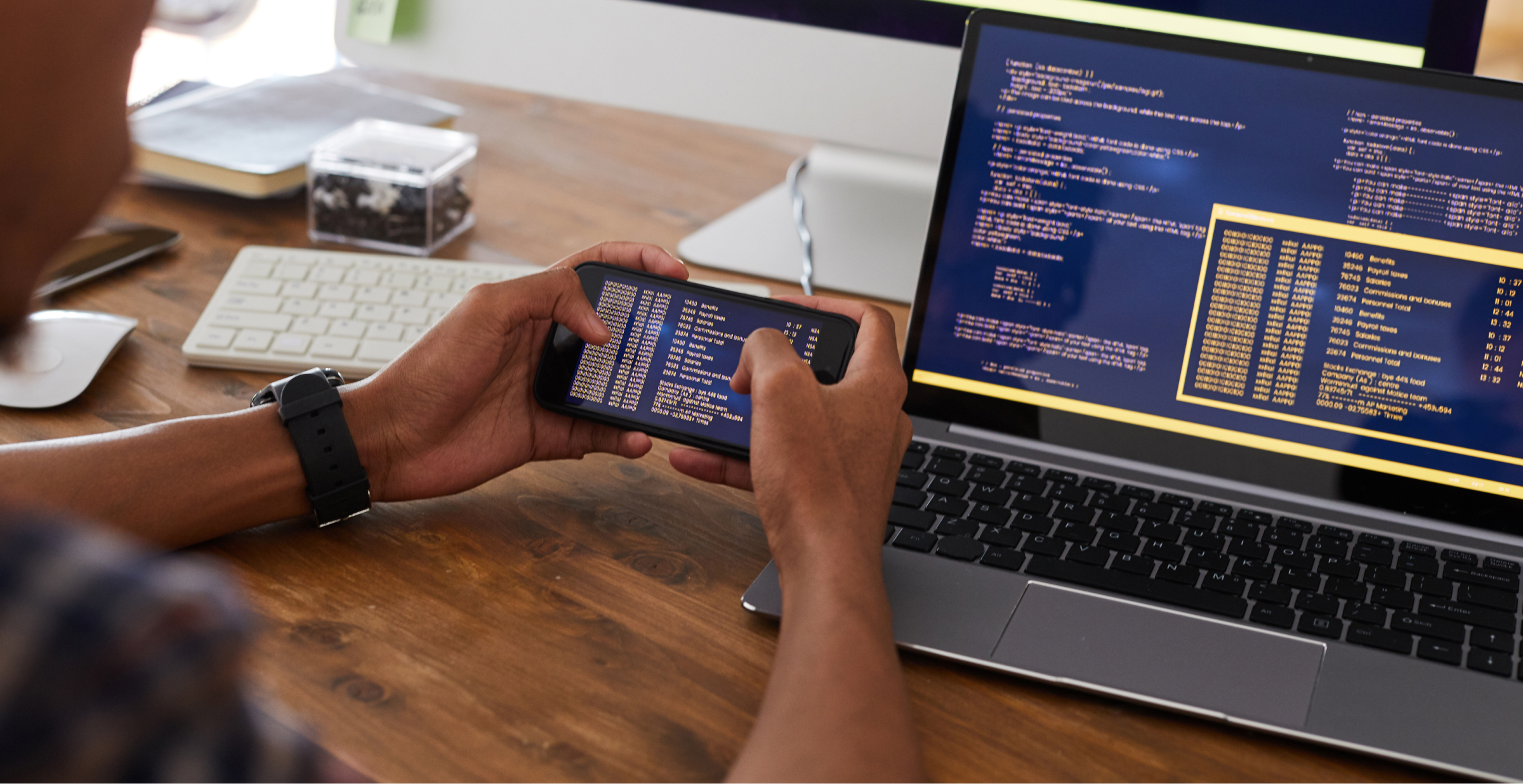 A person coding on multiple screens, using a phone and laptop.