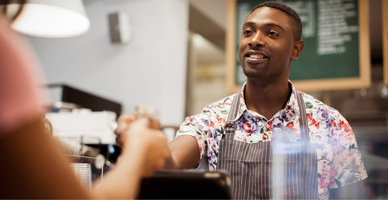 Smiling barista handing a payment terminal to a customer in a coffee shop, emphasizing customer service.