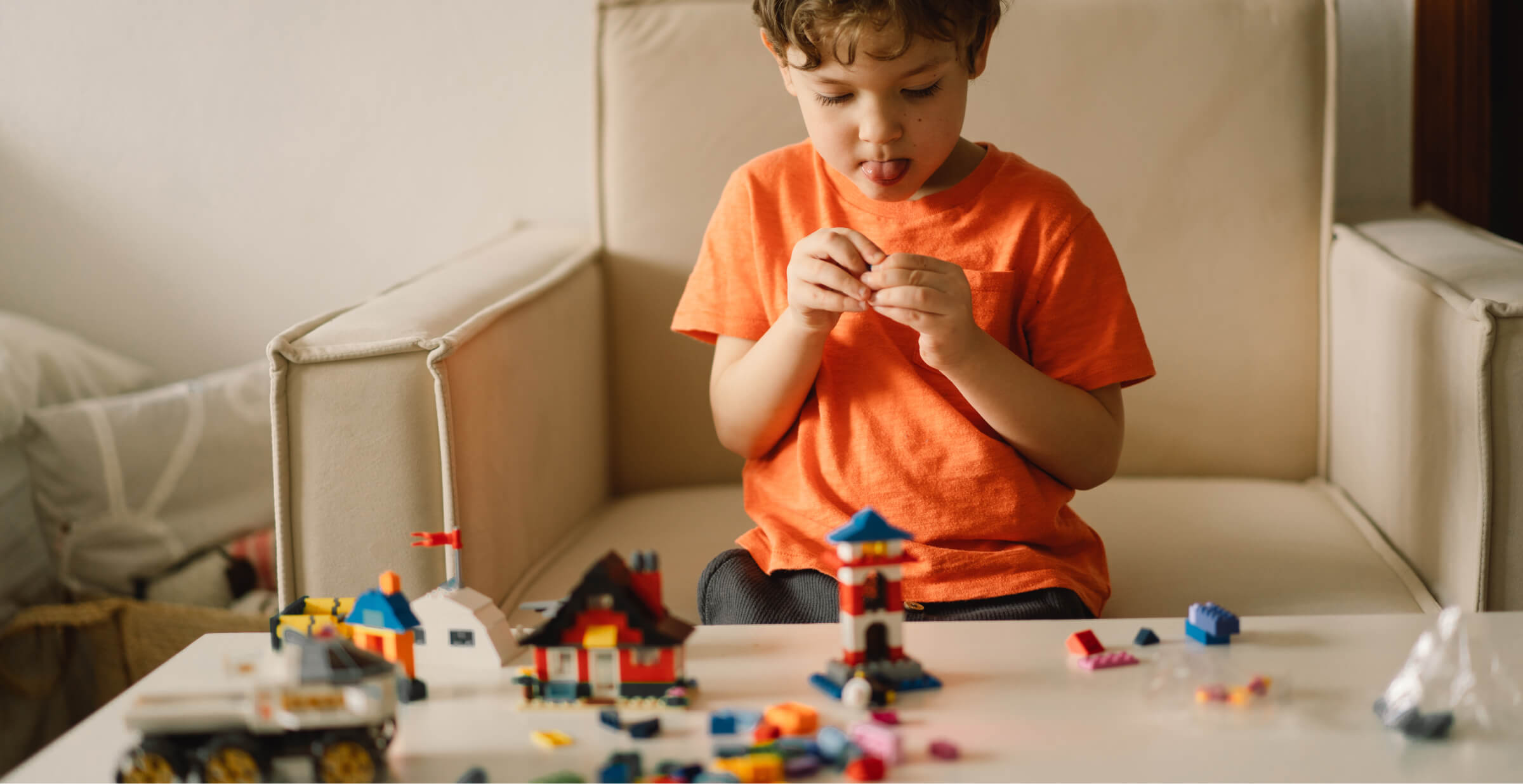 Young boy in an orange shirt focused on building with colorful blocks, developing creativity and fine motor skills.