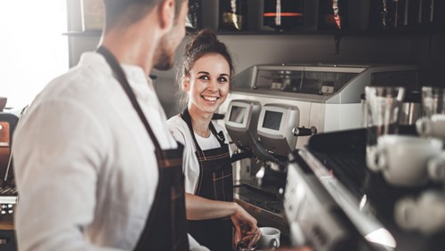 A cheerful man and woman collaborate in a coffee shop, showcasing teamwork and a friendly atmosphere.