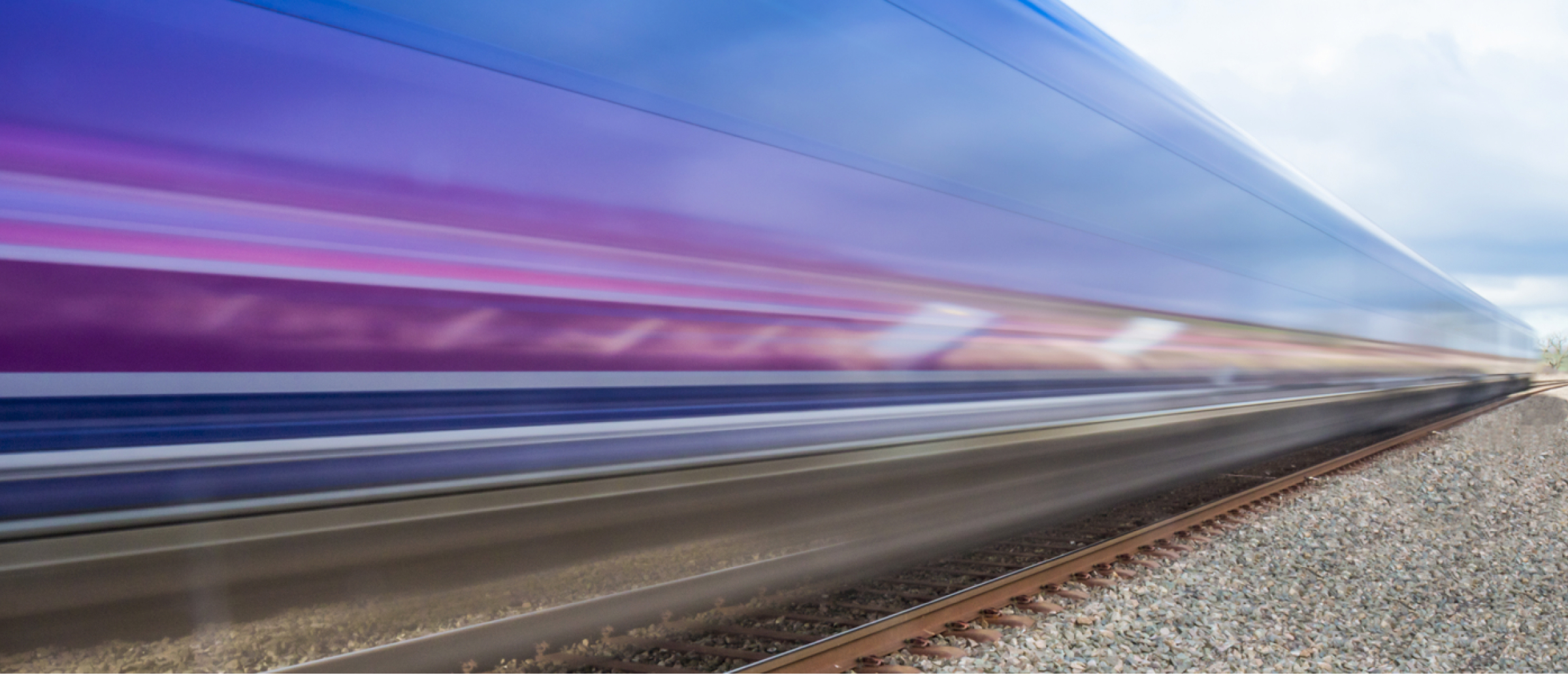 A high-speed train captured in motion, creating a blurred effect as it travels along the tracks. The vibrant colors of the train, including purple and blue, streak across the image, emphasizing speed and modern transportation.