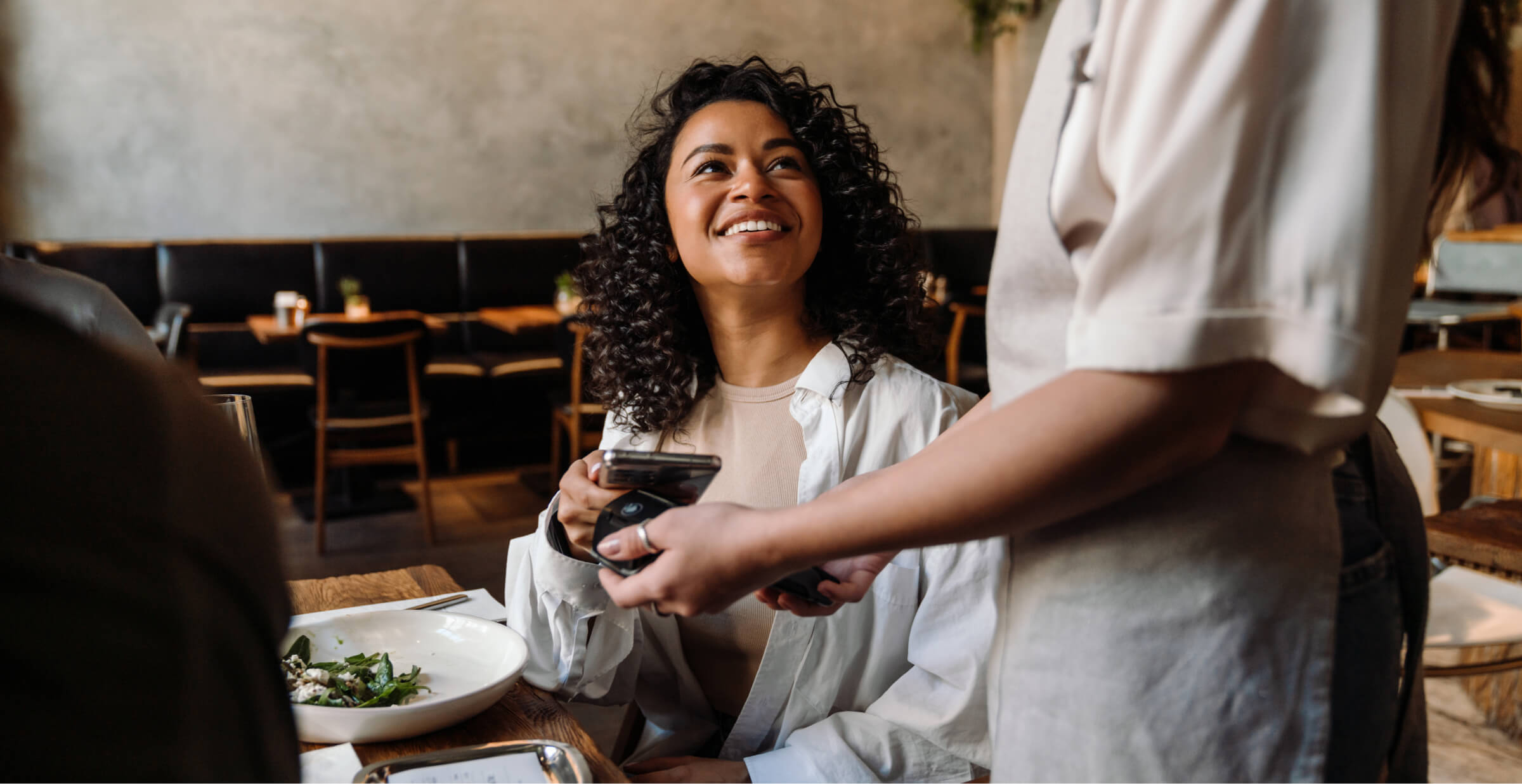 Customer paying with smartphone at a restaurant, smiling at the server.