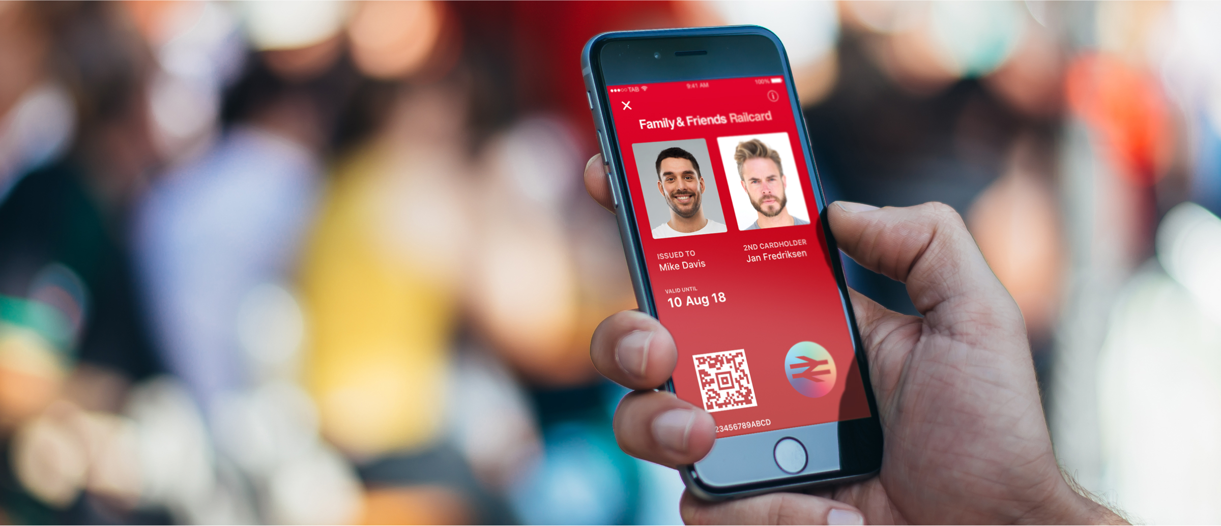 A person holding a smartphone displaying a digital Family & Friends Railcard. The card shows two cardholders' photos, names, expiration date, and a QR code for scanning, with a vibrant red background. The scene captures a busy outdoor environment with blurred figures in the background.