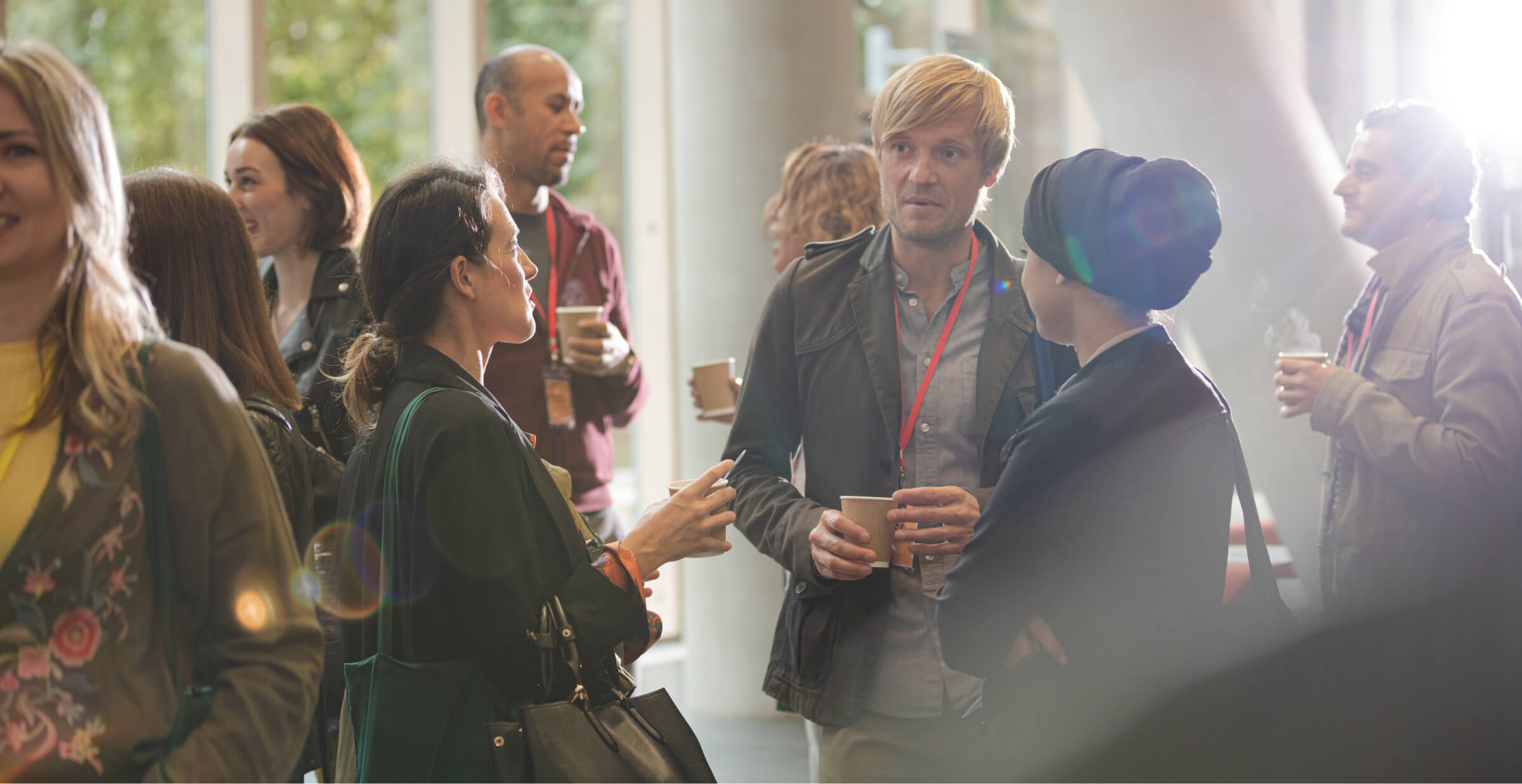 A group of people engaging in conversation during a conference break, with name badges and coffee cups.