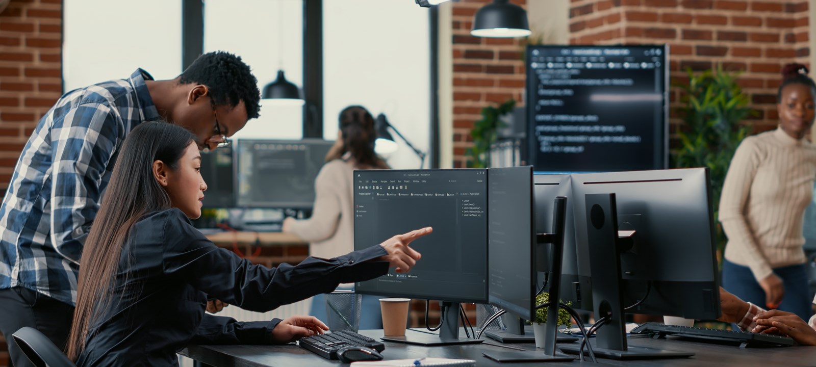 A diverse team of professionals working in an office setting, collaborating on data tasks at multiple computer workstations, with code displayed on monitors and a modern workspace environment.
