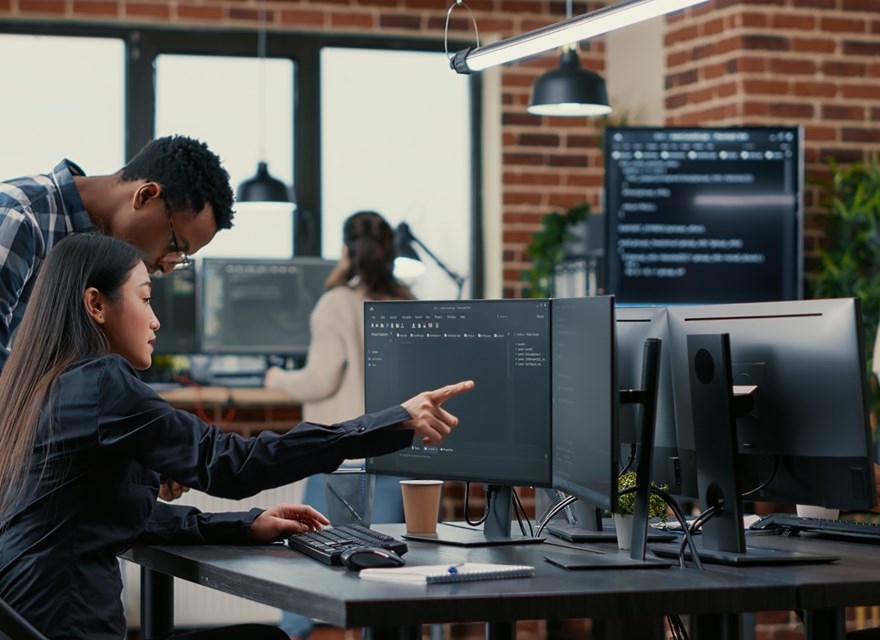 A diverse team of professionals working in an office setting, collaborating on data tasks at multiple computer workstations, with code displayed on monitors and a modern workspace environment.