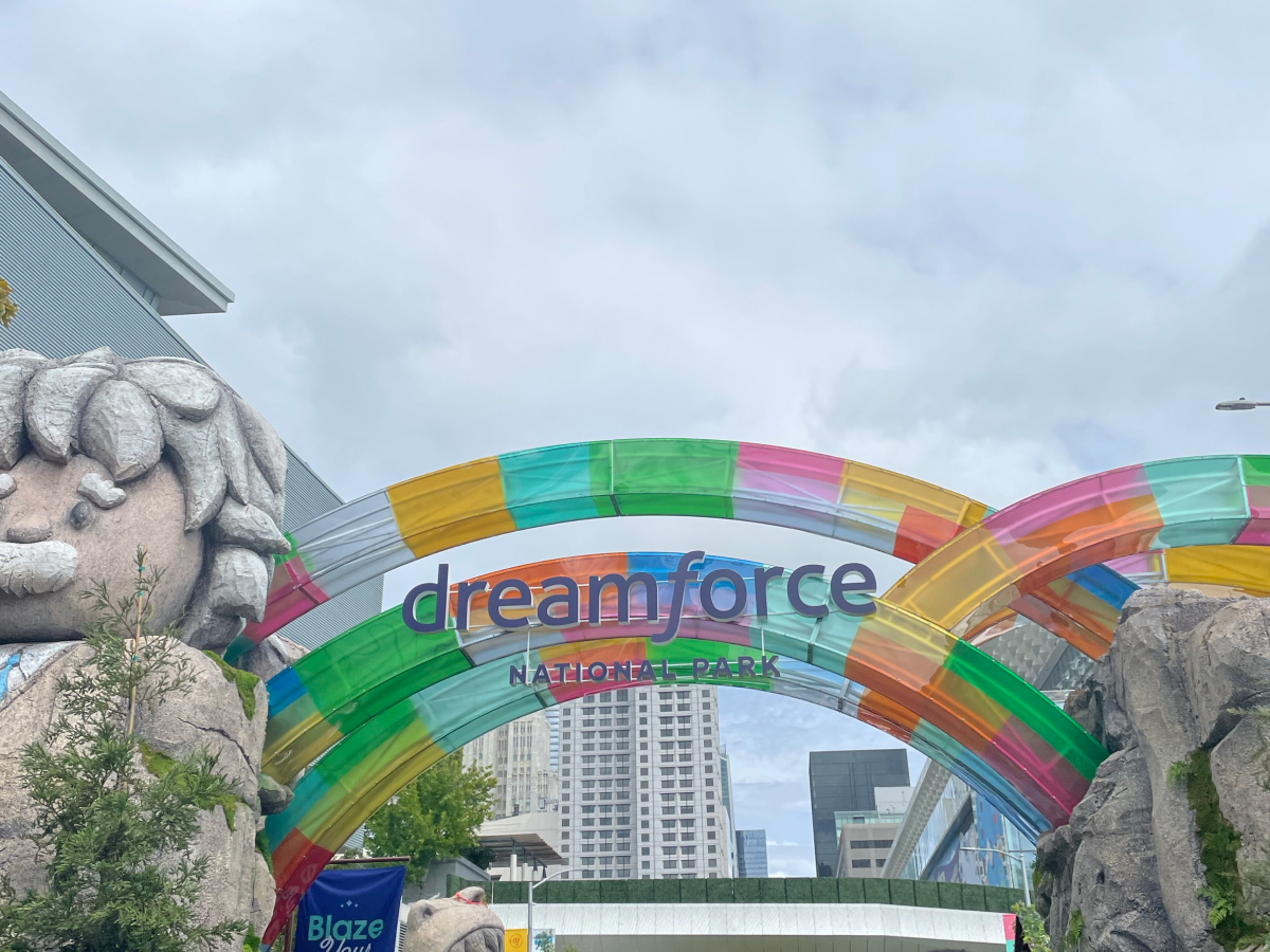 Colorful arches at the entrance of Dreamforce 2024 National Park, with a large stone statue and vibrant decorations set against a cityscape backdrop.