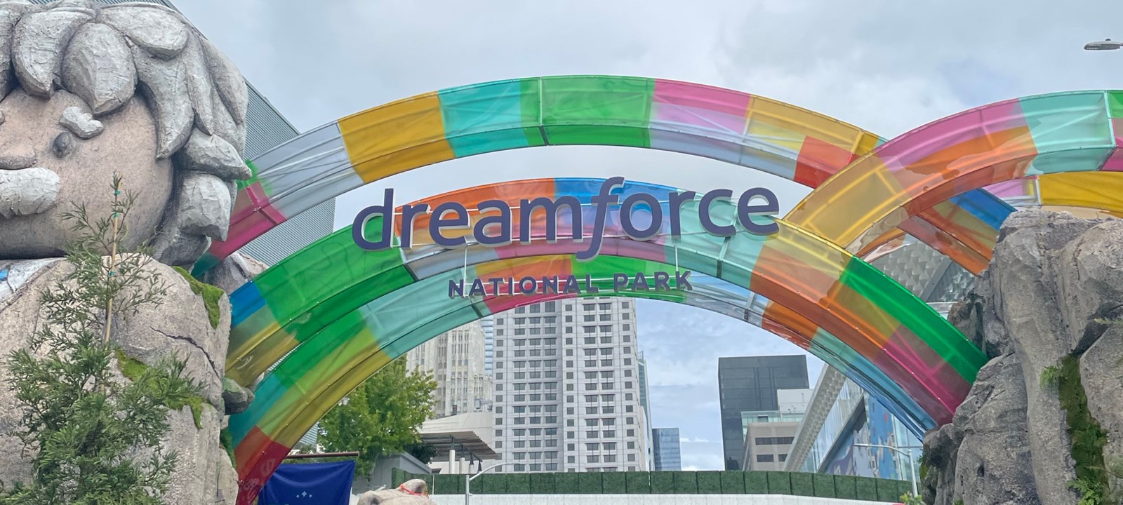 Colorful arches at the entrance of Dreamforce 2024 National Park, with a large stone statue and vibrant decorations set against a cityscape backdrop.