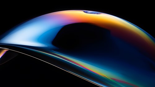 A sleek, abstract image featuring a smooth, curved shape with a gradient of blue, orange, and yellow tones, set against a black background, creating a futuristic and reflective visual effect.