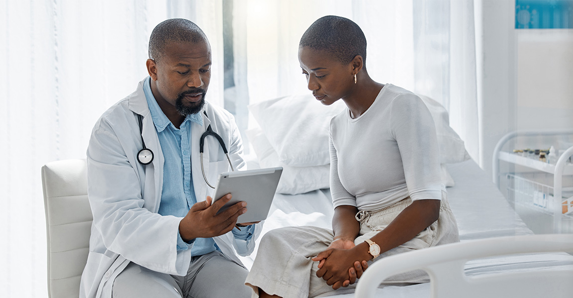 Black male doctor showing Black female patient the Novartis app in a clinic room